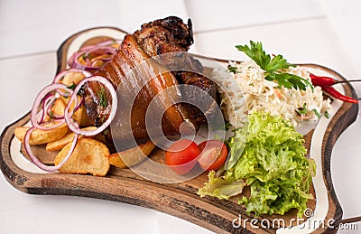Baked pork knuckle with sauerkraut, potatoes, onions and greens on a wooden cutting board Stock Photo