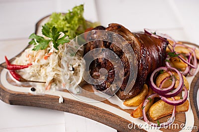 Baked pork knuckle with sauerkraut, potatoes, onions and greens on a wooden cutting board Stock Photo