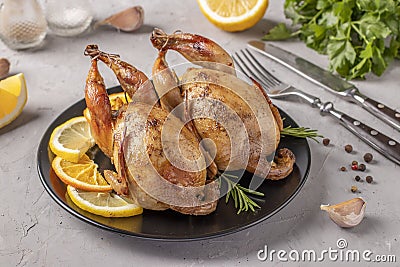 Baked quails with lemon and orange served on a dark plate on a gray background Stock Photo