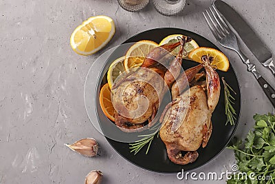 Baked quails with lemon and orange served on a dark plate on a gray background, Copy space Stock Photo