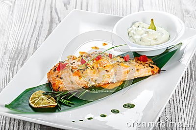 Baked salmon with cheese sauce, rosemary and lemon on wooden background. Hot fish dish. Stock Photo