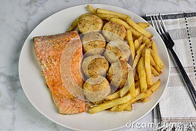 baked salmon with scallops served with a side of fries Stock Photo