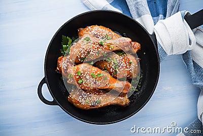 Baked spicy chicken legs with sesame and parsley in cast iron frying pan on blue wooden background top view Stock Photo