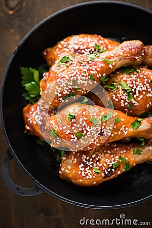 Baked spicy chicken legs with sesame and parsley in cast iron frying pan on dark wooden background Stock Photo