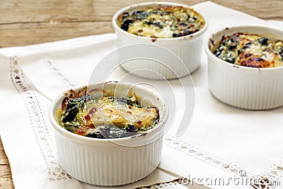 Baked spinach with cheese in small casserole servings, white nap Stock Photo