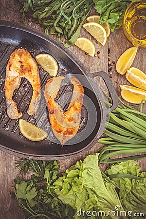 Baked steak trout fish in cast-iron form, around greens, leaves, Stock Photo