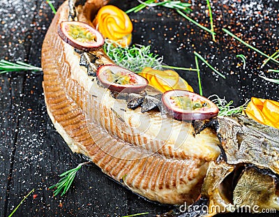 Baked sturgeon fish with rosemary, lemon and passion fruit on plate on wooden background close up. Stock Photo