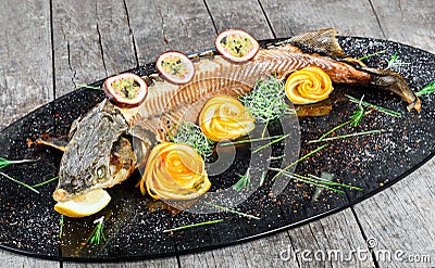 Baked sturgeon fish with rosemary, lemon and passion fruit on plate on wooden background close up. Stock Photo