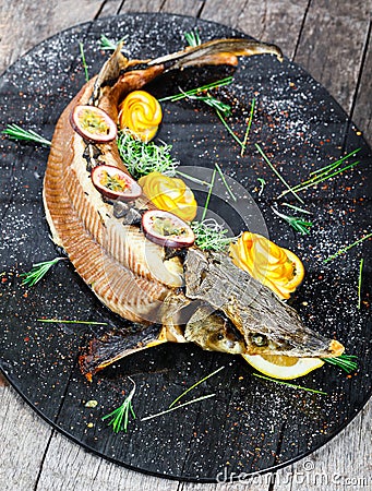 Baked sturgeon fish with rosemary, lemon and passion fruit on plate on wooden background close up. Stock Photo
