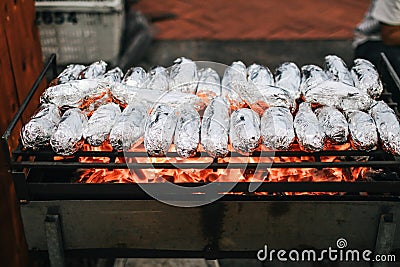 Baked sweet potatoes wrapped with aluminum foil roasting.Burned by heat on the fireplace, with bamboo, with a tongs placed on the Stock Photo