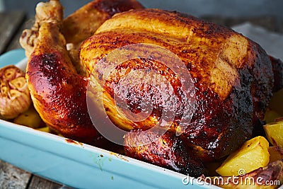Baked whole chicken in blue casserole on dark gray old wooden table, roasted meat with potatoes. Side view, close up Stock Photo