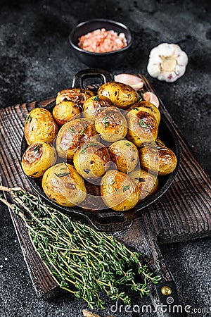 Baked youg potato with thyme in a pan Black background. Top view Stock Photo