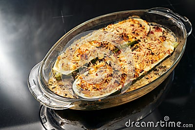 Baked zucchini filled with vegetables, feta cheese and parmesan in a glass casserole fresh from the oven, dark background with Stock Photo