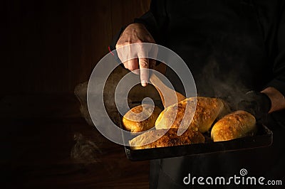 The baker bakes hot dog buns. Kitchen scraper in the chef hand. Space for advertising on a dark background Stock Photo