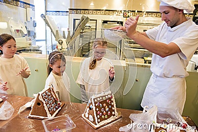 Gingerbread house baking in the run up to Christmas. Baker shows children how to sprinkle powdered sugar over gingerbread house Editorial Stock Photo