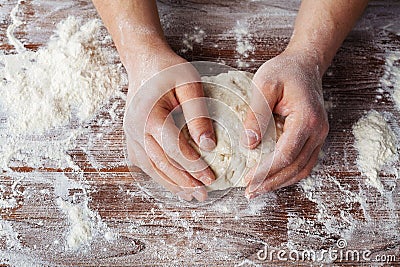 Baker prepares the dough on a wooden table, male hands knead the dough with flour Stock Photo