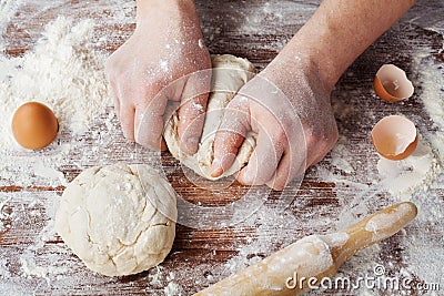 Baker prepares the dough on a wooden table, male hands knead the dough with flour Stock Photo