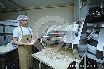 At the bakery: baker working a dough forming machine forming dough for baking baguette Editorial Stock Photo
