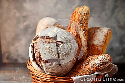 Bakery products in a wicker basket. Round homemade bread, long loaf with seeds, vegan bread without yeast. Wooden background Stock Photo