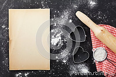 Baking background with flour, rolling pin, paper sheet and heart shape on kitchen black table from above for Valentines day. Stock Photo