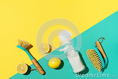 Baking soda, lemon, mustard powder and bamboo brushes against household chemicals products over yellow background. Top Stock Photo
