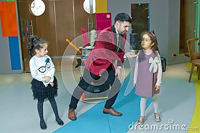 An illusionist and kids is holding a dove in his hands. The magician shows a performance . Focus-illusionist shows children Editorial Stock Photo