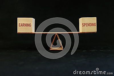 Balance and equal earning and spending and budgeting concept. Earnings and spending word in seesaw in dark black background. Stock Photo