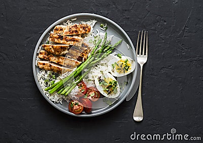 Balanced healthy lunch - rice, asparagus, grilled chicken, boiled egg on a dark background, top view Stock Photo