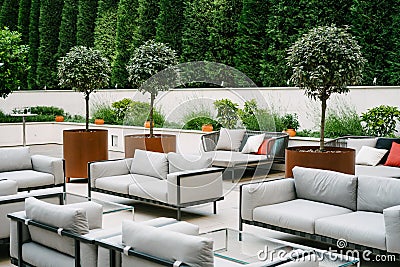 Balcony with white sofas and glass tables, surrounded with green trees and flowerpots. Stock Photo