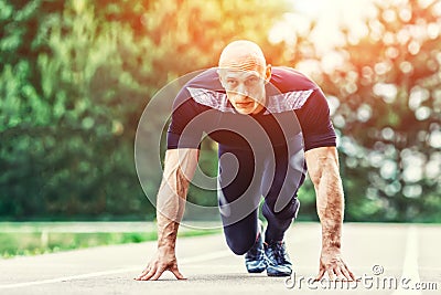 Bald Athletic Man in Running Start Position and Looking Into the Distance in stadium. Stock Photo