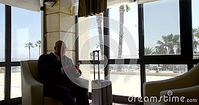 A bald business man in glasses and a classic suit sits in a chair behind a Desk in the reception room, looks at the Stock Photo