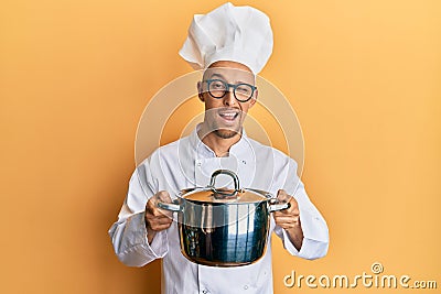 Bald man with beard wearing professional cook holding cooking pot winking looking at the camera with sexy expression, cheerful and Stock Photo