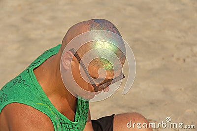 A bald and unusual young man, a freak, with a shiny bald head and round wooden glasses on the background of the beach and the sea Stock Photo