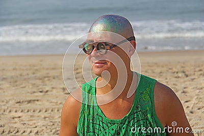 A bald and unusual young man, a freak, with a shiny bald head and round wooden glasses on the background of the beach and the sea Stock Photo