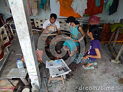 BALI, INDONESIA - CIRCA 2014: A batik workshop worker shows a tourist how to make a battic design on a piece of canvas near the to Editorial Stock Photo