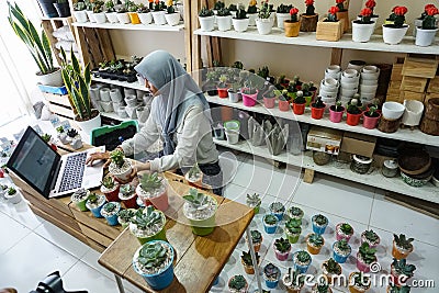 BALI/INDONESIA-MAY 25 2019: A Muslim businesswoman is selling succulent plants on internet. She has a clean and white workshop. Editorial Stock Photo