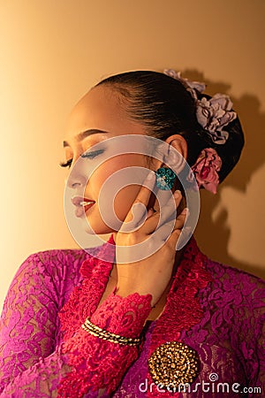 Balinese Women showing their green earrings while wearing a pink traditional dress Stock Photo