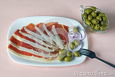 Balkan cuisine . White plate with slices of prsut and green olives on pink pastel background Stock Photo