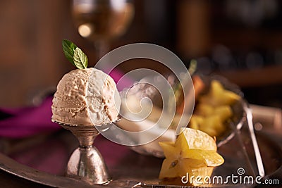 A ball of caramel ice cream with a mint leaf in an ice-cream bowl with carambola fruit on the background of a plate with sliced ch Stock Photo