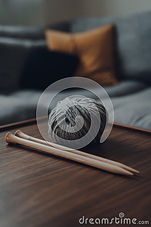 Ball of grey chunky wool yarn and a pair of large wooden knitting needles on a table Stock Photo