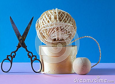 Ball of string on a wooden pedestal with a pair of ornate scissors on a blue and pink background , concept of hobbys and pastimes Stock Photo