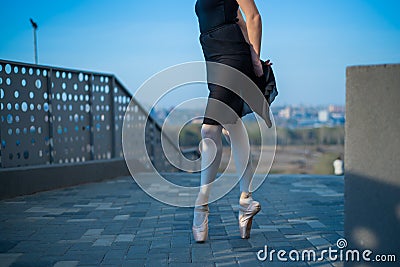 Ballerina in ballet legs in shoes and black tutu dancing by the fence. Beautiful young woman in black dress and pointe Stock Photo