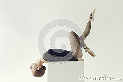 ballerina in a black bodysuit lies on a cube with her head thrown back and one leg stretched up Stock Photo