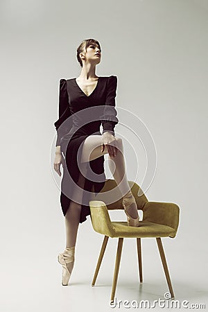 ballerina in a black dress stands showing a deflection and plasticity and putting her foot on a chair Stock Photo