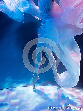 Ballerina dancing underwater in pointe and waved dress, soft blurred focus in water. Stock Photo