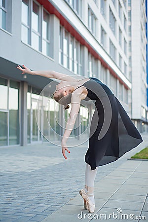 Ballerina in a tutu posing in front of a multi-storey residential building. Beautiful young woman in black dress and pointe shoes Stock Photo