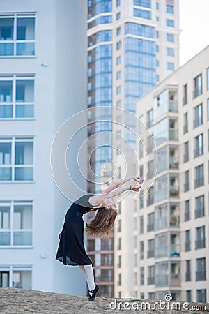 Ballerina in a tutu posing at a multi-storey residential building. Beautiful young woman in black dress and pointe shoes with Stock Photo