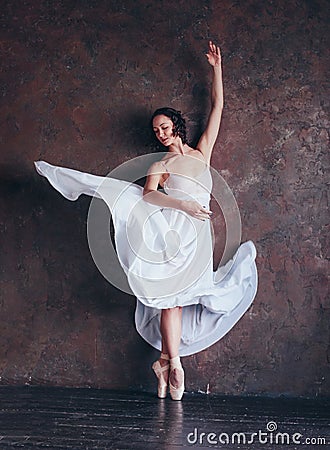 Ballet dancer ballerina in beautiful thin flying white dress is posing in dark loft studio Stock Photo