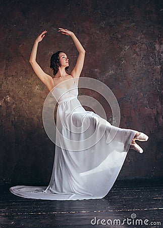 Ballet dancer ballerina in beautiful thin flying white dress is posing in dark loft studio Stock Photo