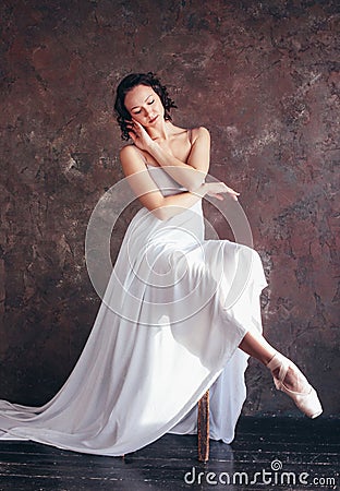 Ballet dancer ballerina in beautiful thin flying white dress is posing in dark loft studio Stock Photo